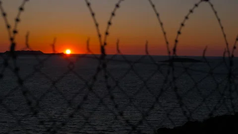 Orange sun setting behind barbed wire over ocean. Stock Footage 332635963