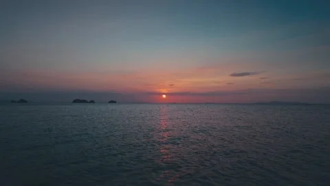 Orange sun sinking into tranquil ocean, setting sun casts warm glow across Stock Footage 312745734