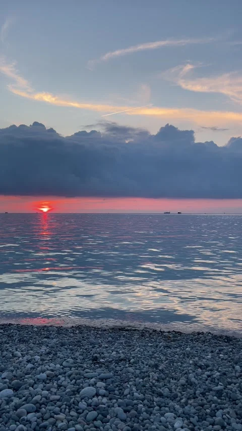Orange sun sinks beneath a dramatic dark cloud bank above a calm sea, casti.. Stock Footage 340024863