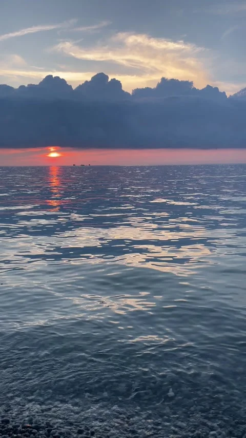 Orange sun slowly sinks under a dramatic bank of storm clouds above gently .. Stock Footage 340559400