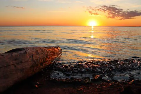 Orange sunset over the river with a log and small wave Stock Photos