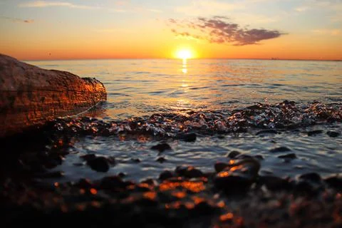 Orange sunset over the river with a log and small wave Stock Photos