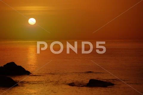 Orange sunset over the sea with rocks Stock Photos