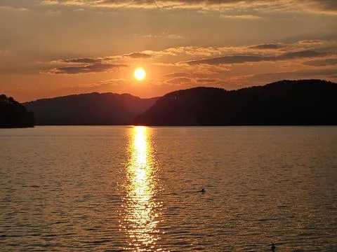 Orange Sunset Reflecting on Lake Between Dark Mountains 스톡 사진