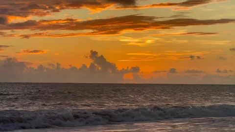 Orange sunset sky with clouds and ocean surface with light waves breaking on the Stock Footage 321407043