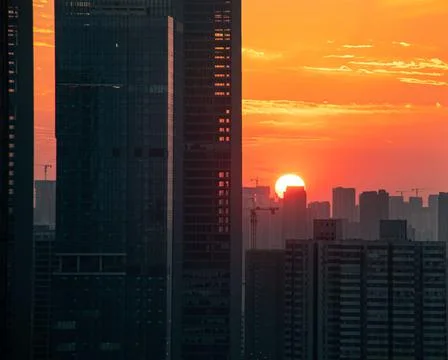 Orange sunset sun disk behind long urban skyscrapers buildings Stock Photos
