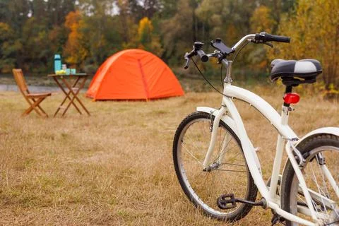 Orange tent set up on grassy lake shore, bicycle in front of it, cycling to.. Stock Photos