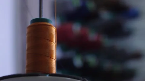 Orange thread rotating on sewing machine spool in textile workshop. Stock Footage 313815370