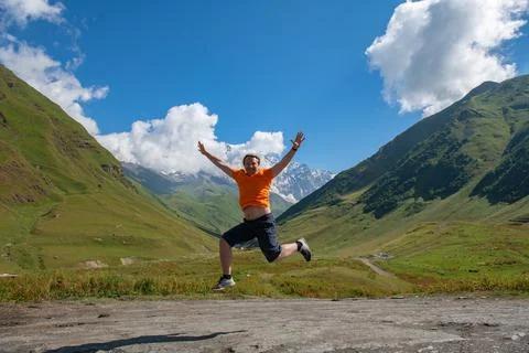 Orange Thrust: Man Takes Flight Amidst Green Mountains and Clouds Foto stock