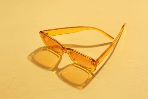 Orange tinted rectangular sunglasses with transparent frames casting shadows  Stock Photos