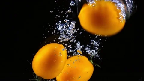 Orange tomatoes dropping into the water and swimming in slow motion. Видео 77180343