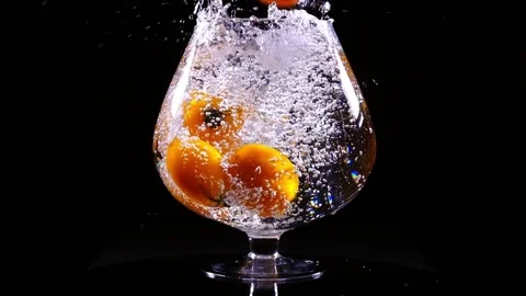 Orange tomatoes with water dropping into the big wineglass in slow motion Видео 77837097