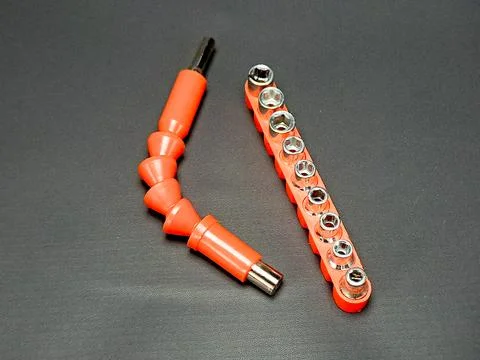 Orange tools including sockets and flexible extension lay on a dark texture.. Stock Photos