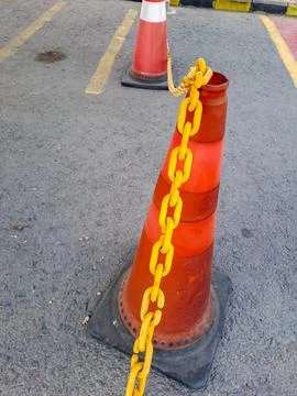 Orange traffic cones connected by a yellow plastic chain on asphalt. Stock Photos