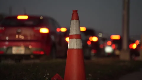 An orange traffic pylon stands on the roadside during evening rush hour with Stock Footage 335161509
