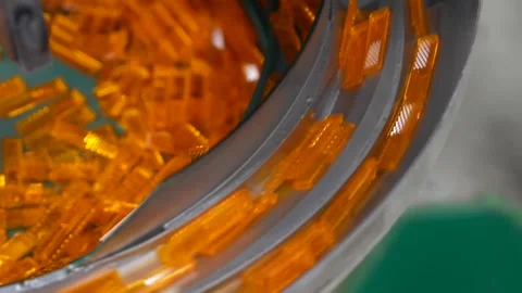 Orange translucent molded plastic parts tumbling inside a vibratory bowl feeder Stockbeeldmateriaal 340901704