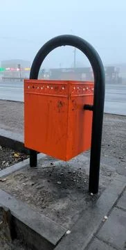 Orange trash bin next to a bus stop on a foggy day. Stock Photos