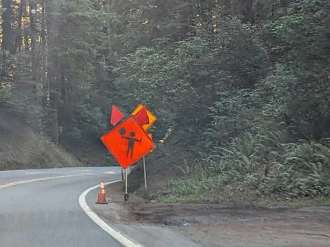 Orange triangular flagger warning sign placed along quiet forest road Photos