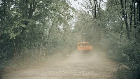 Orange Truck Stirring Up Dust on Gravel Wood Road Stock Footage