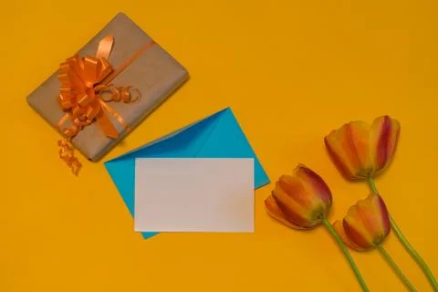 Orange tulips, gift box, empty card and evenlope on bright yellow background. Foto stock