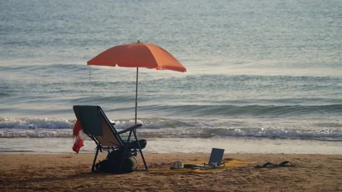 An orange umbrella on the beach, next to a deckchair and a beach blanket wi.. Video stock 229507347
