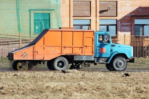 Orange urban sweeper cleans road from dirt with a round brush in the spring. Stock Photos