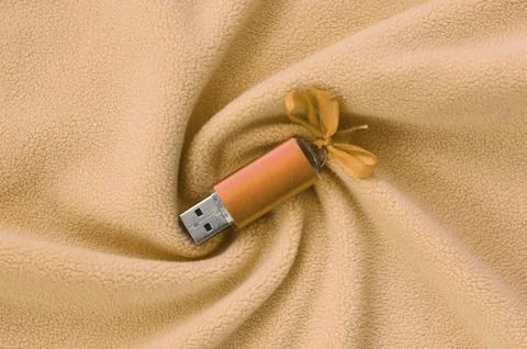 Orange usb flash memory card with a bow lies on a blanket of soft and furry l Stock Photos