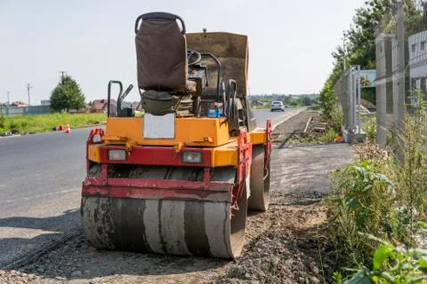 Orange Vibration roller compactor standing on a ground near asphalts road at Stock Photos