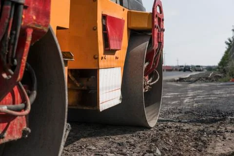 Orange Vibration roller compactor standing on a ground near asphalts road at Stock Photos
