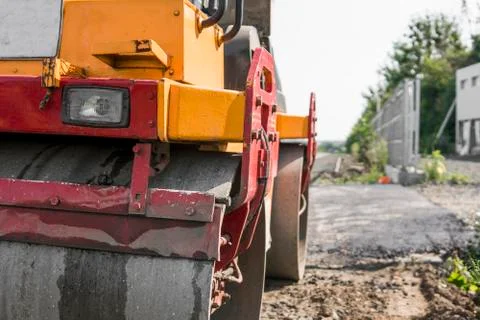 Orange Vibration roller compactor standing on a ground near asphalts road at Stock Photos
