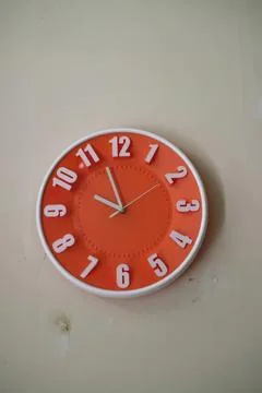 Orange wall clock with white numbers showing time Stock Photos