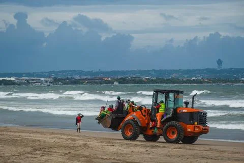 Orange Wheel Loader Transporting Workers on a Sandy Shoreline Fotos de archivo