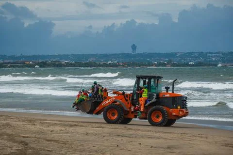 Orange Wheel Loader Transporting Workers on a Sandy Shoreline Photos