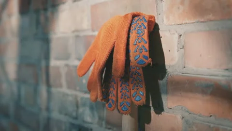Orange Work Gloves with Blue Pattern Hanging on Brick Wall in Sunlight Stock Footage 306025387