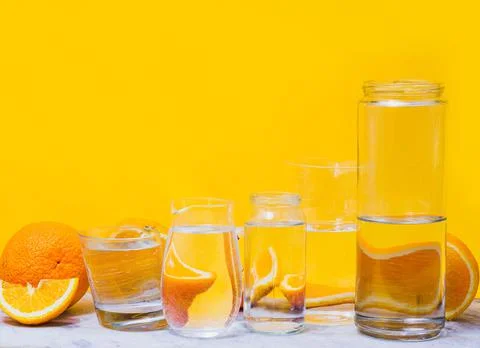 Oranges distorted through the glasses with water. Yellow background. Summer c Stock Photos