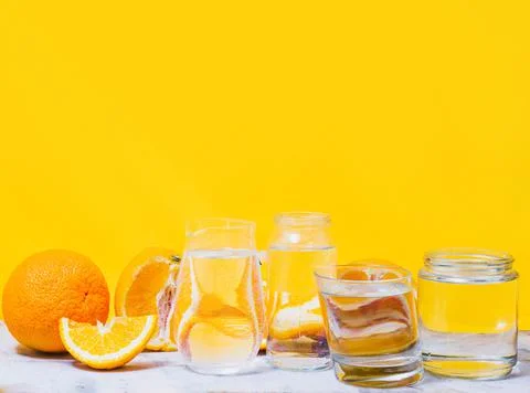 Oranges distorted through the glasses with water. Yellow background. Summer c Stock Photos