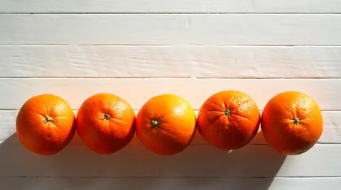 Oranges, five on a row on an old white wooden table Stock Photos