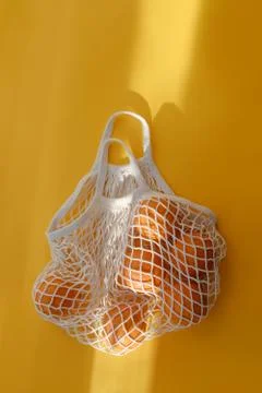 Oranges lie in string bag on bright yellow background and hard sunshine. The Stock-Fotos