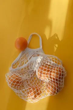 Oranges lie in string bag on bright yellow background and hard sunshine. The Stock Photos