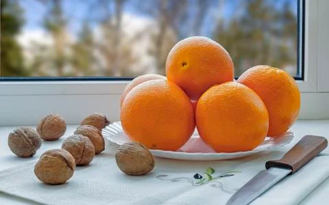 Oranges on a plate on the sill of the window. Stock Photos