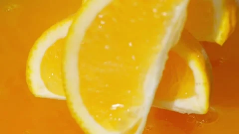 Oranges slices splashing into bright orange juice, creating vibrant waves Stock Footage 288114620