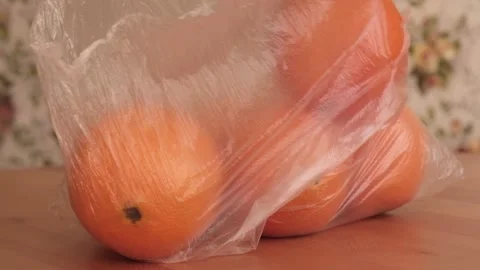 Oranges in a transparent plastic bag fall on a wooden table. Stock Footage 150386106