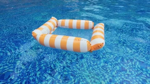 Orange‑white striped inflatable float drifting on blue swimming pool water Stock Footage 344832123