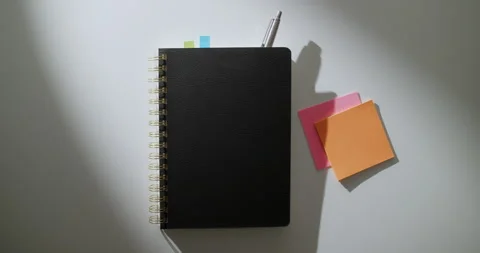 Orbit Around Black Notebook and Pen on White Table in Dramatic Light Stock Footage 346695404