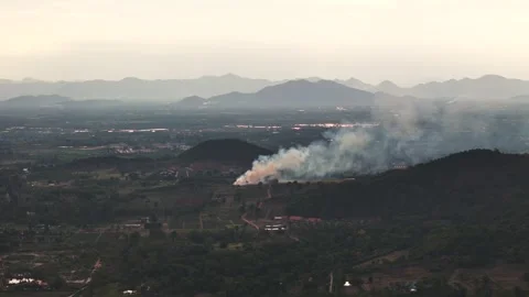 Orbit drone shot of fire smoke in valley surrounded by mountain at sunset Stock Footage 311267256