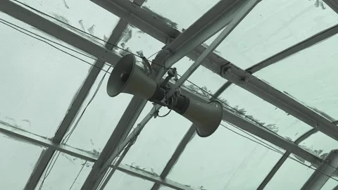 Orbit shot of public address loudspeaker mounted beneath steel roof structure Stock Footage 340975901