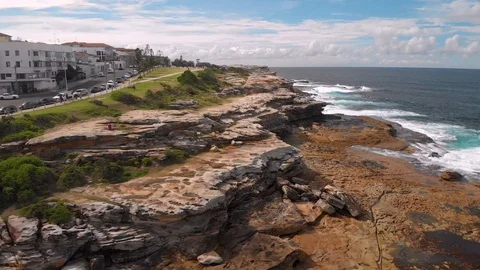Orbiting around cliffs on a rocky coastline with waves crashing into them, 4K Stock Footage 105664684