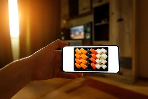 Order sushi set via the mobile app on your smartphone from home. Stock Photos