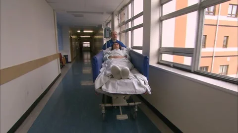 Orderly wheeling patient down corridor Stock Footage