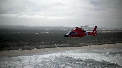 OREGON - 5.9.2025 - A US Coast Guard helicopter flies along a forested beach in Stock Footage 312863044